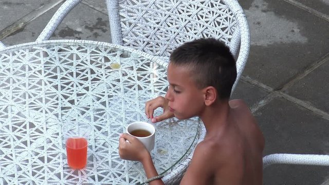 Cute little naket boy sitting at the table drinking juice 