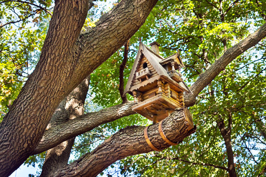 Wooden small hut birdhouse on a tree among the leaves. Carved wooden birdhouse in the form of a log house