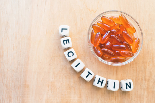 Lecithin gel pills in a round glass bowl and with the word Lecetin from the letters of cubes on a light wooden background. Soy and sunflower lecithin benefits for skin, digestion, lower cholesterol.