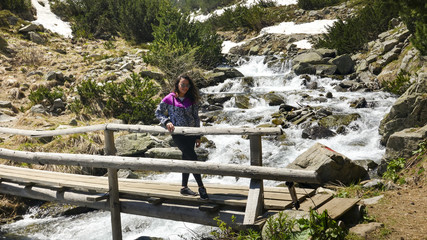Fototapeta na wymiar Mountaineering girl standing on old grey wooden bridge during the spring waters flowing from melted snow