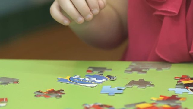 Close-up of unidentified little child collect picture from puzzles sitting at desk in kindergarten
