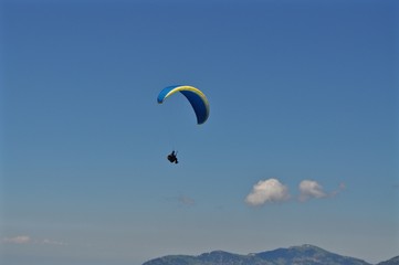 Gleitschirmfliegen: Blauer Gleitschirm fliegt am blauen Himmel über Berge, Schweiz