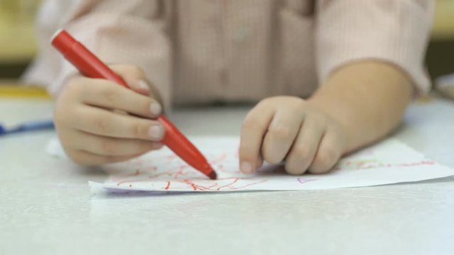 Close-up of hands of unknown little girl draw and paint pictures with felt-tip sitting at desk in the kindergarten