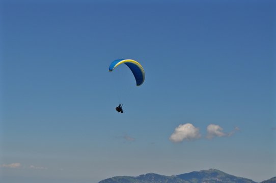 Gleitschirmfliegen: Blauer Gleitschirm fliegt am blauen Himmel &uuml;ber Berge, Schweiz