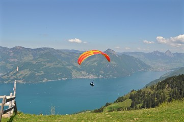 Gleitschirmfliegen über dem Vierwaldstättersee inmitten der Schweizer Berge in der Zentralschweiz / Bunter Paragleiter / Gleitschirm fliegt über den See, Schweiz