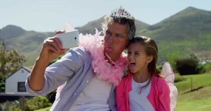 Smiling father and daughter in fairy costume taking selfie with mobile phone 