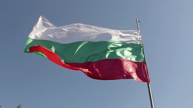 Bulgarian national flag waving on flagpole in blue sky. Bulgaria, 