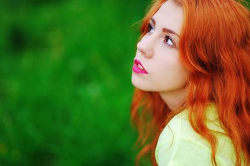 Naklejka premium Cute red-haired girl resting on the green lawn and looks to side, closeup.