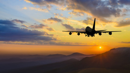 Fototapeta na wymiar Plane taking off over mountain range at sunset