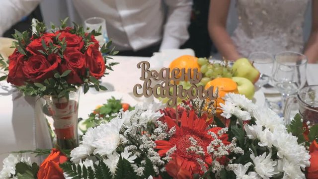 Close-up wedding table of unidentified newlyweds with bouquets and inscription in Russian - On Wedding Day