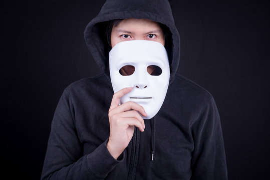 Mystery man holding white mask for hide his face. Anonymous social masking or halloween concept.