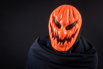 Mystery man with orange pumpkin evil mask on black background, Halloween night costume concept