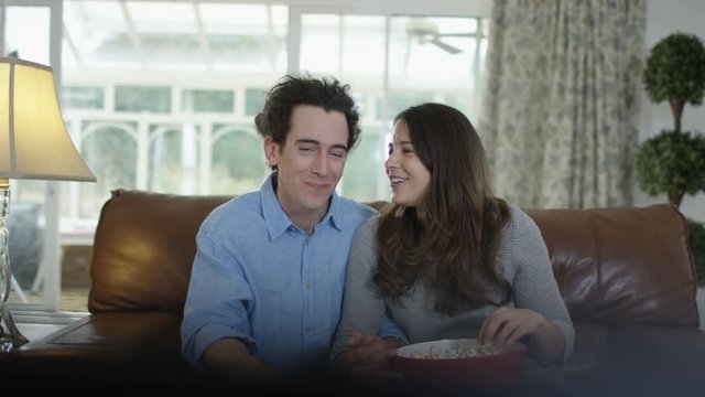  Couple watching TV & eating popcorn, reacting to the action on screen