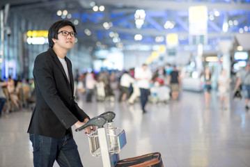 Young asian man with his luggage on airport trolley waiting for check in at airline counter in the international airport terminal, business travel concept