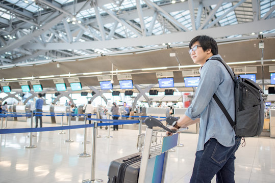 young asian waiting for check in and drop his luggage at airline check-in counter inside the international airport terminal, travel lifestyle concept