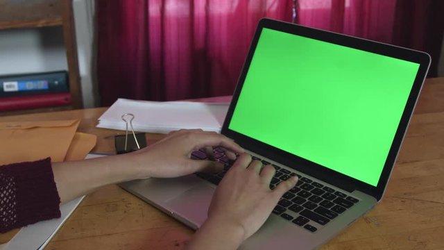 Typing on laptop with green screen at a desk