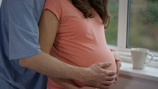  Pregnant couple relaxing at home, both with their hands on baby bump