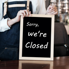 Hand holding closed sign chalkboard in font of cafe counter background, food and drinks