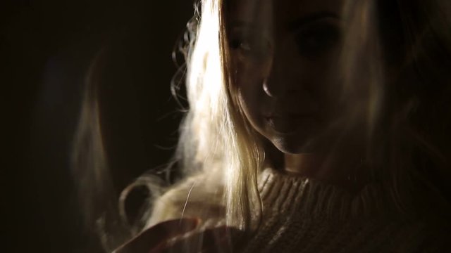 Close-up of silhouette of beautiful woman with long eyelashes and long curly hair, illuminated by artificial light.