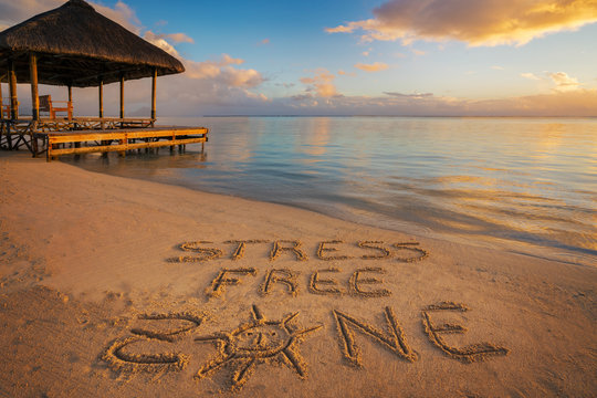 Foreground written in the sand "stress free zone" at sunset in Mauritius Island with Jetty silhouette and Fishermen's boats in the background.
