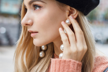 Close up detail of beautiful young blonde woman dressed in pink sweater with gorgeous earrings made...