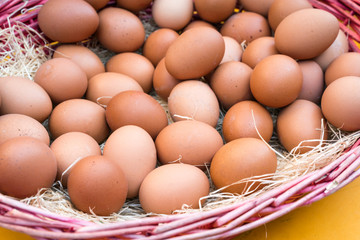 Brown chicken eggs leaning on straw in wooden basket.