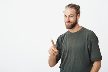Happy bearded handsome man with trendy hairstyle pointing with finger upside with smiling face....