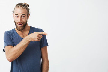 Beautiful strong man with good-looking hairstyle and beard in blue shirt pointing a side with surprised face expression. Copy space for advertisement - obrazy, fototapety, plakaty