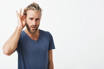 Good-looking swedish guy with beard and cool hairstyle holding hand near ear showing he don't hear...