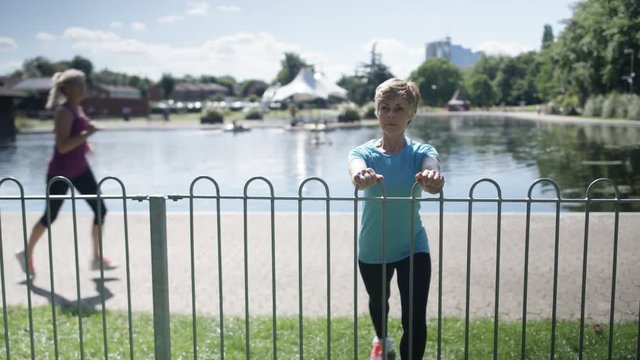  Healthy & active mature lady running in the park stops to do some stretches