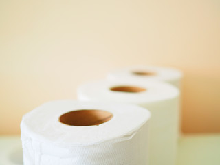 Small white tissue paper rolls, stacked altogether in row, with pale yellow pink painted wall background, close up perspective top view