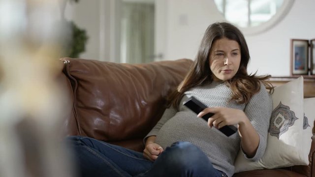  Pregnant woman watching TV at home & feeling baby kicking