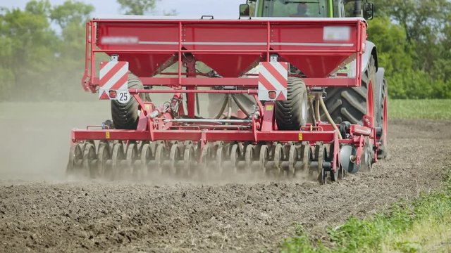 Agricultural tractor with trailer seeder working on plowed field. Sowing machine driving on plowed field. Sowing process on agricultural field. Agricultural industry. Rural farming. Sowing seeds