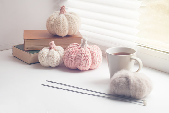 Autumn cozy window composition, Window at home. Book, cup, needles, yarns ball and knitted pumpkins, toned photo