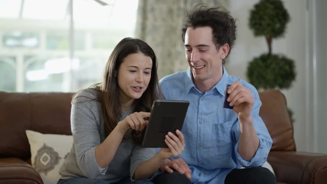  Cheerful couple with tablet & credit card shopping online at home