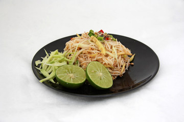 Thai vermicelli eaten Spicy blend with Mackerel in the black dish, Food decoration with lemon, chili, and mango on white background.