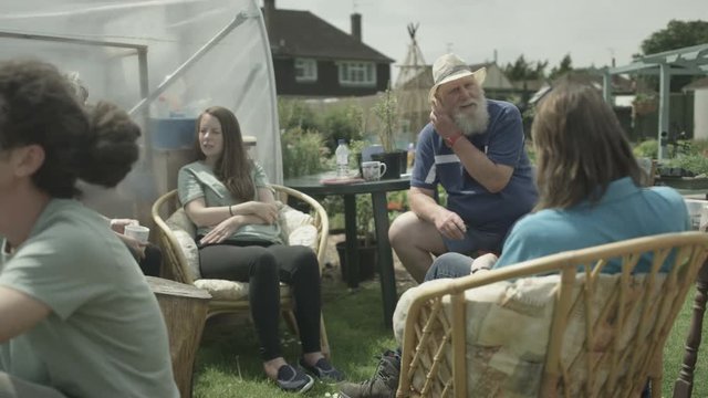  Cheerful group relaxing & chatting with drinks in shared community garden