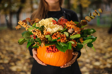 Pumpkin with beautiful bouquet of autumn flowers in woman hands