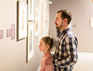 interested father and daughter regarding exhibition of photos in the museum