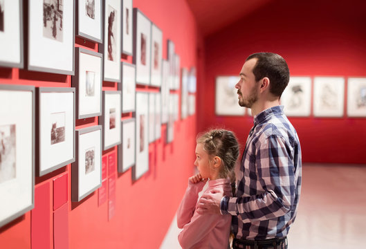 Father and daughter looking at exhibition of photos in museum