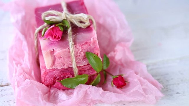 Pink  handmade soap  with roses on pink crumpled paper on a light wooden plank background