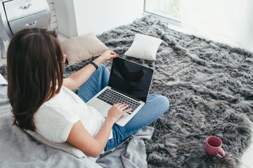 Beautiful young woman working from home on a laptop sitting on the floor in the room, back view