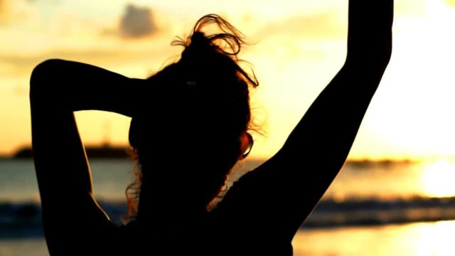 Silhouette of the woman standing next to the sea at the evening, steadycam shot
