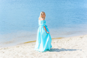 Fototapeta na wymiar Portrait of middle age plus size woman on the beach near the sea. Blonde hair lady on the beach. Single girl in long dress. Woman walking barefoot on white sand of island.