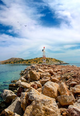 Small lighthouse from metal and big rocks on the ground under cloudscape . Greece