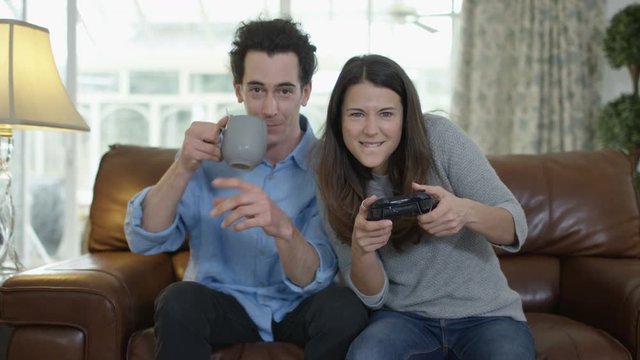  Competitive woman playing video games at home, with boyfriend beside her.