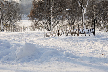 Fototapeta premium Snow-covered trees, stones, fences and benches in the city park