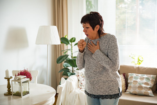 Sick Mature Woman With Sore Throat, Standing In Living Room At Home. Catching Cold, Having Cough.