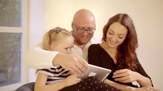 happy parents and little daughter are watching photos in a tablet, smiling and laughing