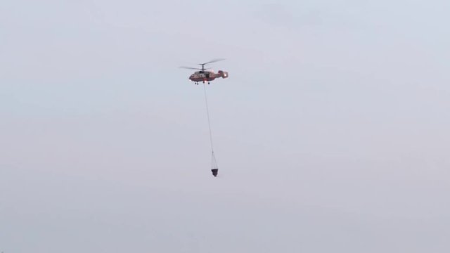 Helicopter Drops Water Fir. A helicopter battles a gigantic wildfire on a dry mountainside, dropping hundreds of gallons of water on the flames. Military helicopter. Emergency